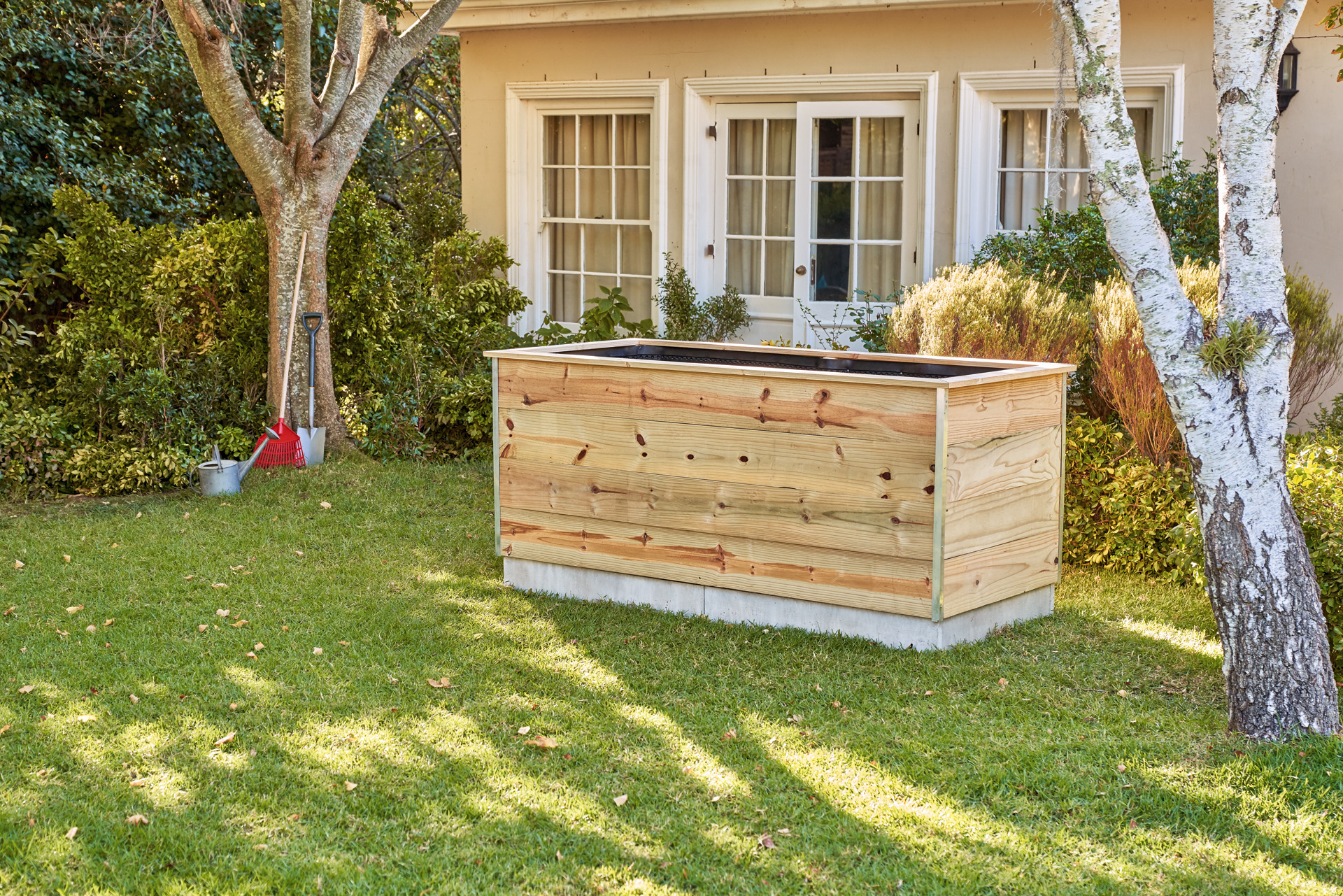 Mesa de cultivo hecha con listones de madera, en el jardín frente a una casa.