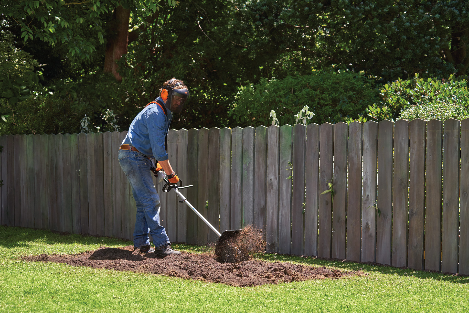 Una persona con equipo de protección cultiva un huerto jardín ecológico con un STIHL KombiSystem con fresadora.