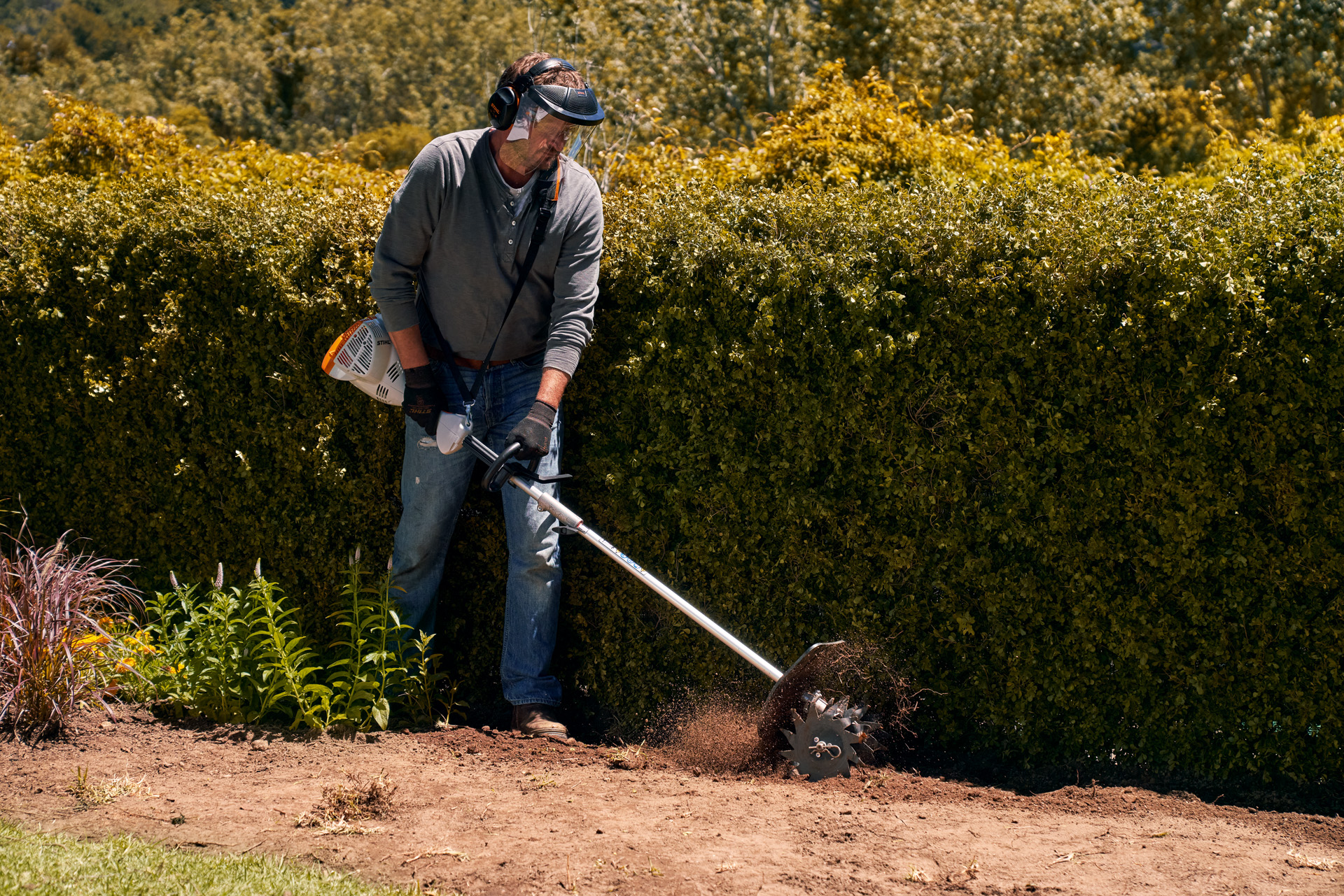 Un hombre con una pantalla y guantes utiliza el STIHL KombiEngine KM 56 RC-E.